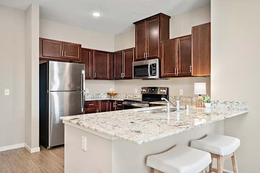 A kitchen with a granite countertop and white stools at The Winslow 62+ Apartments, West St Paul