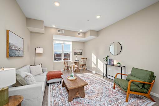A living room with a white couch, a green chair, and a rug at The Winslow 62+ Apartments, West St Paul