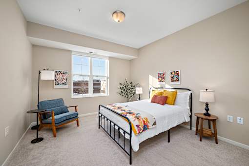 A bedroom with a bed, chair, and lamp at The Winslow 62+ Apartments, West St Paul, Minnesota