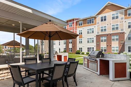 a patio with an umbrella and a table with chairs and a grill at The Winslow 62+ Apartments, Minnesota