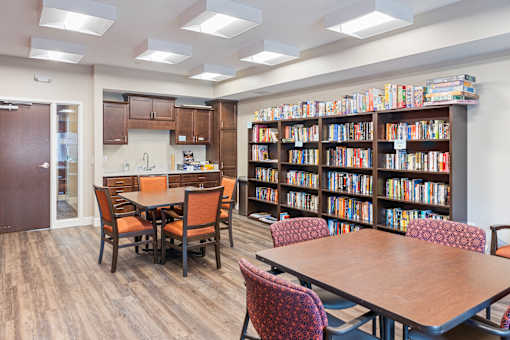 a library with tables and chairs and a kitchen and library shelves at The Winslow 62+ Apartments, West St Paul, Minnesota