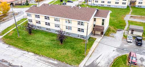A large building with a brown roof is surrounded by a grassy area and a parking lot.
