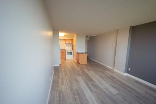 A room with wooden flooring and a small kitchenette in the background.