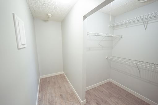 A white room with a wood floor and a white closet with shelves.