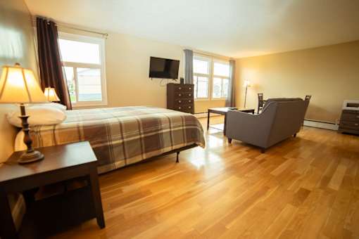 A bedroom with a bed, a chair, a desk, and a lamp.