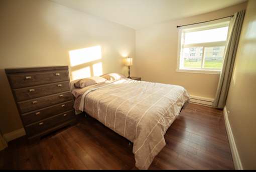 A bedroom with a bed, dresser, and window.