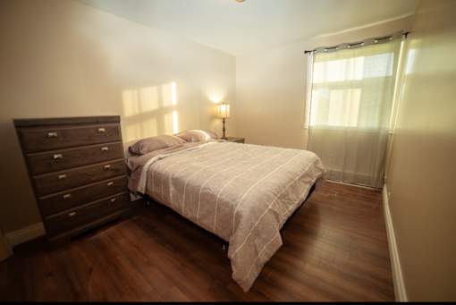 A bedroom with a bed, nightstand, and window with curtains.