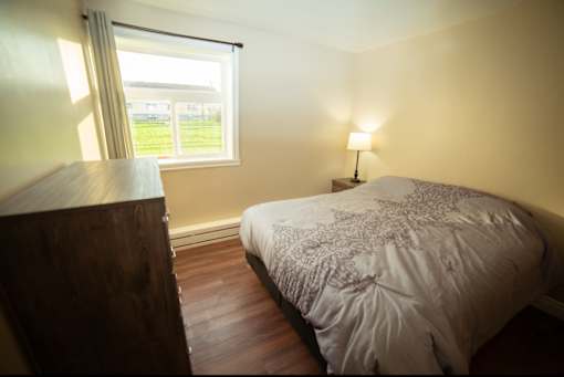 A bedroom with a bed, wooden dresser, and a window with a view of the outside.