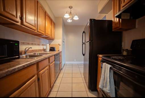 A kitchen with a black refrigerator and brown cabinets.