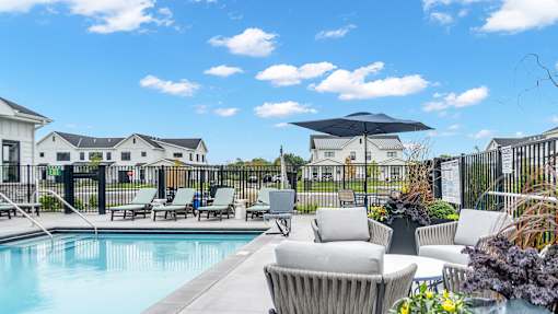 A pool surrounded by chairs and umbrellas with houses in the background.