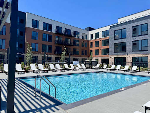 A pool surrounded by sun loungers in front of apartment buildings.