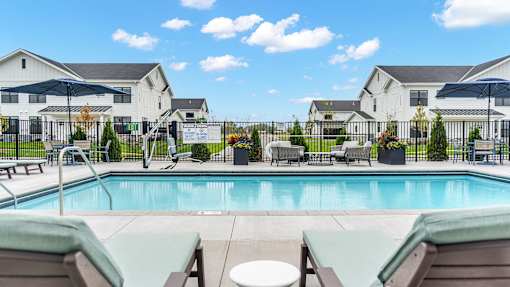 A pool with lounge chairs and umbrellas in front of a white building.