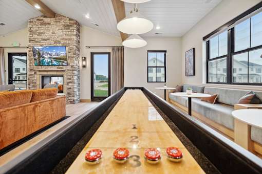 A shiny wooden table with red and white decorations is in the middle of a room with a stone fireplace and a large window.