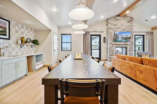 A long wooden table is in the middle of a room with a stone pillar and a couch.