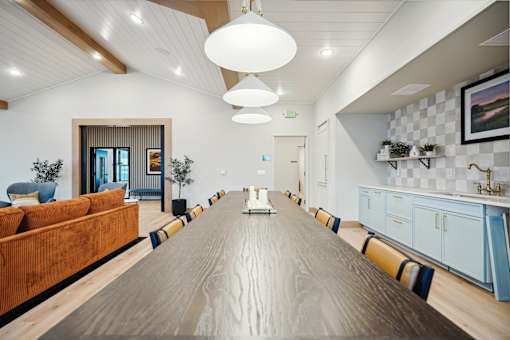 A long wooden table is in the middle of a room with a blue couch and a white chair.