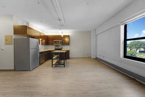 A kitchen with a refrigerator, microwave, and a table with a chair.