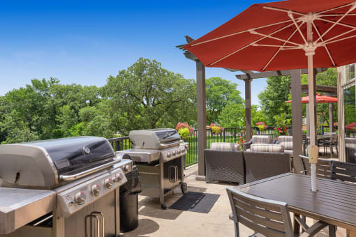 a patio with barbecue grills and tables with umbrellas