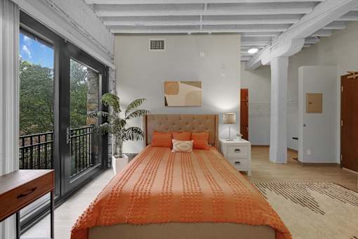 A bedroom with a large bed and a balcony with a view of trees.