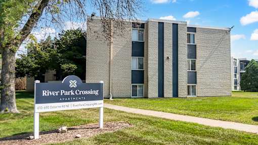 A sign for River Park Crossing Apartments stands in front of a building.