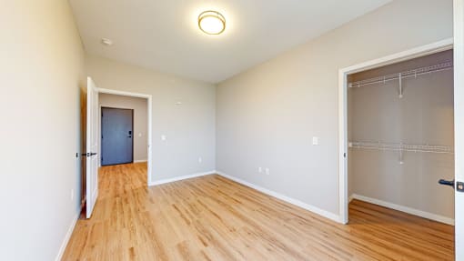 a bedroom with a door to a closet and a hard wood floor at Ardor on the Bluffs South Loop Residences Apartments, Bloomington, Minnesota