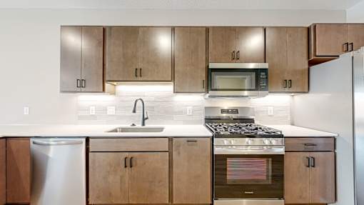 a kitchen with wooden cabinets and stainless steel appliances at Ardor on the Bluffs South Loop Residences Apartments, Bloomington, Minnesota