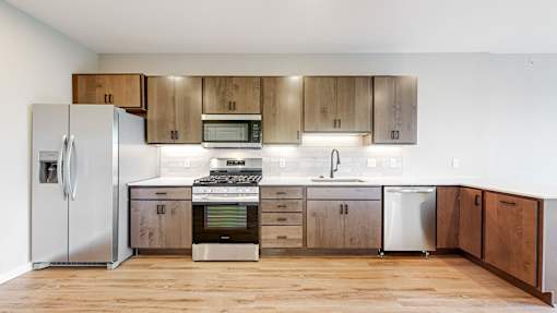 a kitchen with stainless steel appliances and wooden cabinets at Ardor on the Bluffs South Loop Residences Apartments, Bloomington
