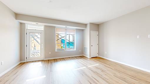 A spacious room with wooden flooring and a view of a balcony through the glass door.
