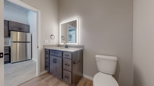 A bathroom with a toilet, sink, and mirror. at Ardor on the Bluffs South Loop Residences Apartments, Minnesota, 55425