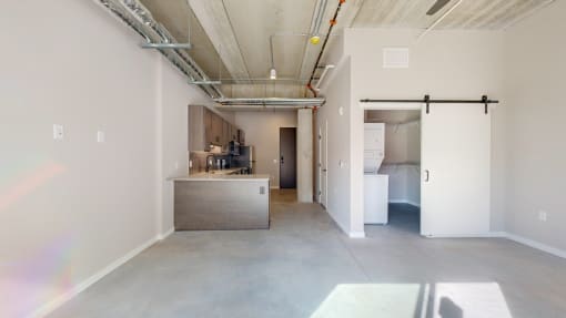 A large empty room with a kitchenette and a doorway leading to another room at Ardor on the Bluffs South Loop Residences Apartments, Bloomington, Minnesota