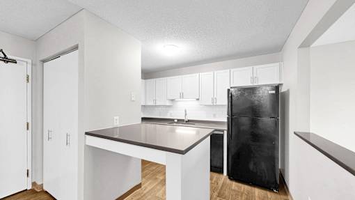 A kitchen with white cabinets and a black fridge.
