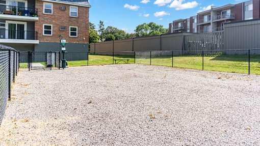 A gravel lot is surrounded by a fence and a brick building.