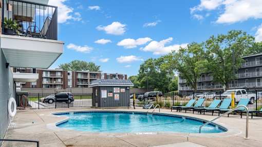 A swimming pool surrounded by lounge chairs and apartment buildings.