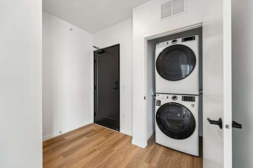 A black door is open to a white wall with a washer and dryer in the other room.