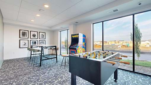 A foosball table is in the middle of a room with chairs and pictures on the wall.