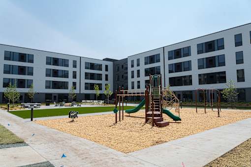 A playground with a green slide and sandbox in front of a building.