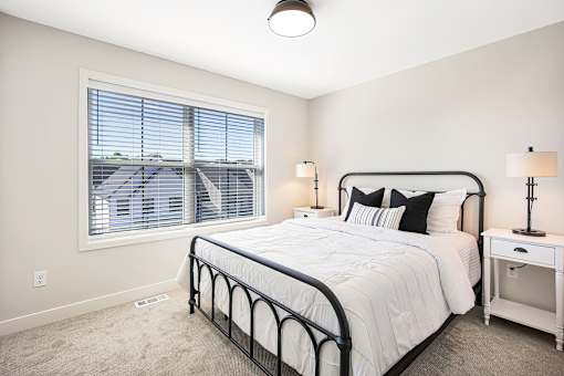 A bedroom with a large bed, nightstand, and window with blinds.