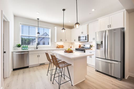 a white kitchen with stainless steel appliances and a white island with two stools