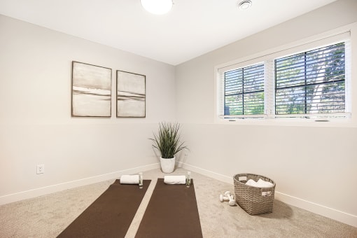 a yoga room with two windows and a brown yoga mat on the floor