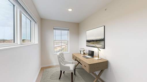 A room with a desk and chair with a window and a painting on the wall.
