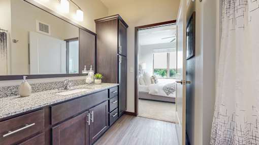 A bathroom with a sink, mirror, and a large open door leading to a bedroom. at Lake Jonathan Flats, Chaska, Minnesota