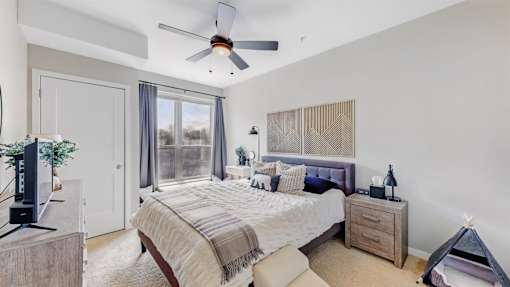 A bedroom with a large bed, a ceiling fan, and a window with curtains.