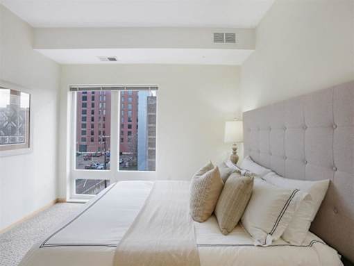 A bedroom with a large bed and a view of a cityscape through the window.at Third North Apartments, Minnesota