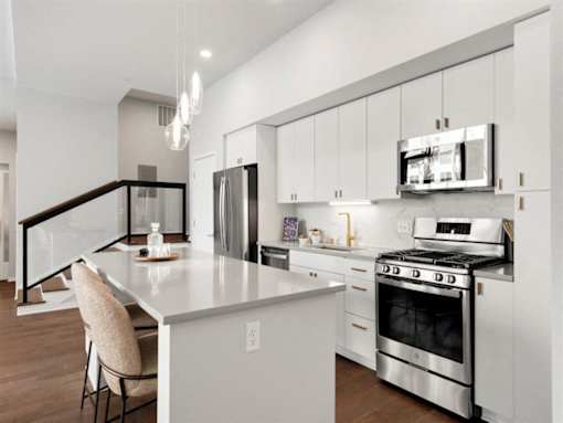 A modern kitchen with a stainless steel refrigerator and oven, and a white island with a chair.at Viridium Apartments, Minneapolis, MN 