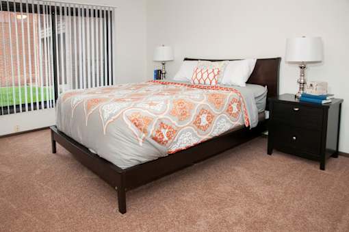 A bed with a white and orange comforter sits in a room with a black nightstand and two lamps.