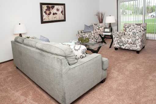 A grey couch with a white pillow and a glass table with a vase of flowers on it.