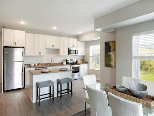 A modern kitchen with white cabinets and a glass table at The Barnum Apartments, Minnesota