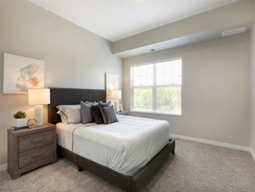 A bedroom with a large bed, nightstand, and window at The Barnum Apartments, White Bear Lake, Minnesota