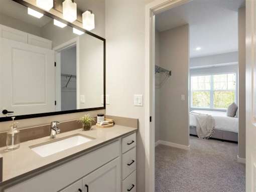 A bathroom with a sink, mirror, and a bedroom in the background at The Barnum Apartments, White Bear Lake, MN,  55110