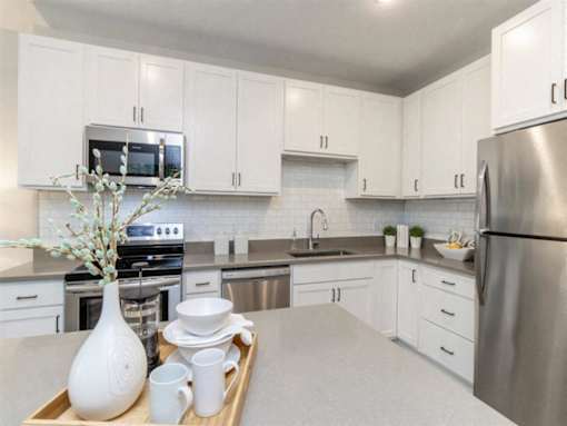 A kitchen with white cabinets and a tray with a vase and dishes on it at The Barnum Apartments, White Bear Lake, Minnesota