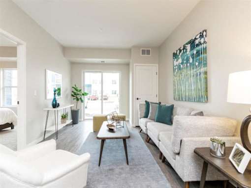 A living room with a white sofa, a white chair, a wooden coffee table, and a painting on the wall at The Barnum Apartments, Minnesota
